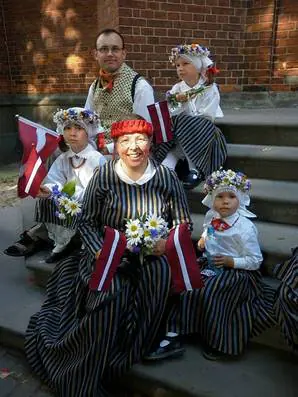 Dziedātāja tautastērpā ar bērniem un Latvijas karodziņiem
